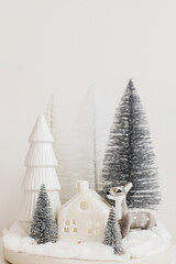 Merry Christmas! Stylish little Christmas trees and reindeer toy on white table. Christmas fairy...