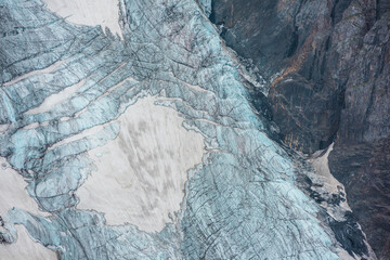 Beautiful mountain landscape with vertical glacier tongue with cracks among rocks. Awesome natural backdrop of large glacier with icefall. Nature texture of mountain glacier with fissures close up.