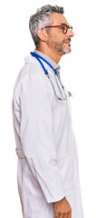 Fototapeta premium Middle age grey-haired man wearing doctor uniform and stethoscope looking to side, relax profile pose with natural face with confident smile.