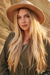portrait of a young woman with long blond hair in a hat on a background of high beautiful sandy rocks. beautiful nature