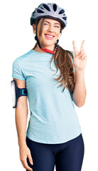 Beautiful caucasian young woman wearing bike helmet smiling with happy face winking at the camera doing victory sign. number two.