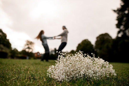 selective focus of bouquet of gypsophila on green grass and couple in love spinning on blurred background
