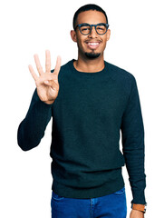 Naklejka premium Young african american man wearing casual clothes and glasses showing and pointing up with fingers number four while smiling confident and happy.