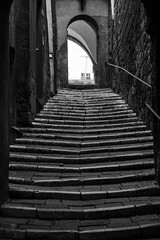 Fototapeta na wymiar A steep, paved street with the stairs and a stone gate