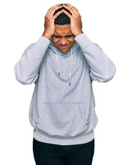 Fototapeta premium Young handsome hispanic man wearing casual sweatshirt suffering from headache desperate and stressed because pain and migraine. hands on head.
