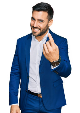Young hispanic man wearing business jacket beckoning come here gesture with hand inviting welcoming happy and smiling