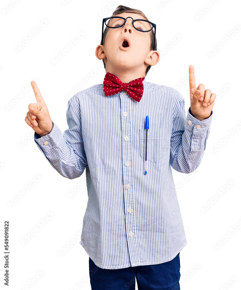 Poster cute blond kid wearing nerd bow tie and glasses amazed and surprised looking up and pointing with fi