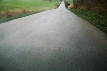 Asphaltierte graue nasse Straße zwischen grünen Feldern am Mittag bei Regen im Winter