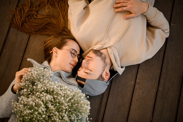 Close-up top view of couple lying together on wooden terrace with eyes closed.