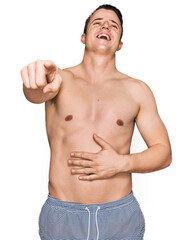 Fototapeta premium Handsome young man wearing swimwear shirtless laughing at you, pointing finger to the camera with hand over body, shame expression