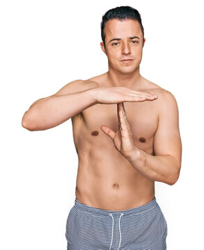 Handsome young man wearing swimwear shirtless doing time out gesture with hands, frustrated and serious face