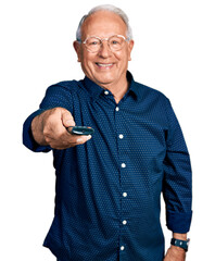 Senior man with grey hair holding television remote control looking positive and happy standing and...
