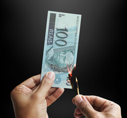 Burning money. Male hand setting a 100 reais bill on fire. Money from Brazil. 3d rendering.