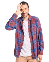 Young handsome man wearing casual clothes doing ok gesture with hand smiling, eye looking through fingers with happy face.