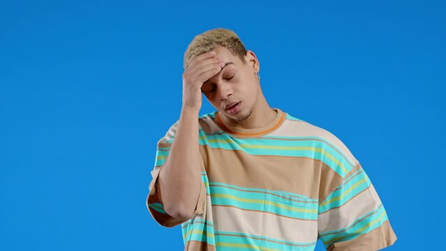 Worried man doing face-palm gesture, like no, I forgot. Disappointed guy feeling sorrow, regret, drama, failure, problems on blue background.