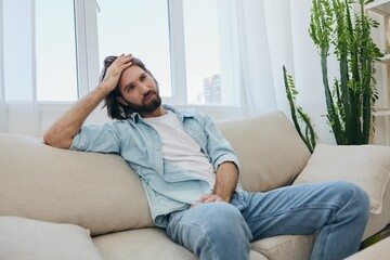 Obraz premium A young male freelancer sits on the couch after a demanding job and rests sadly leaning on the couch. 