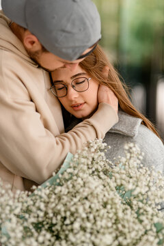 close-up of young woman in glasses with bouquet and man hugging her head