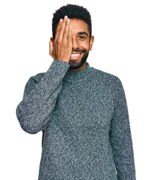 Young african american man wearing casual clothes covering one eye with hand, confident smile on face and surprise emotion.