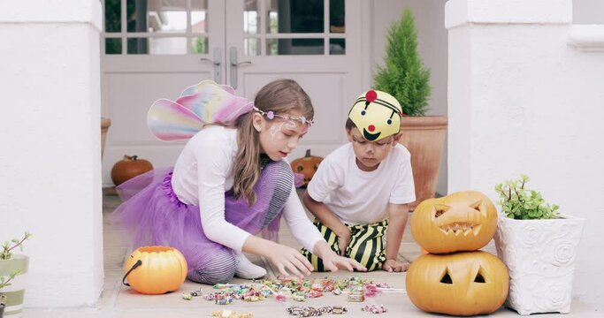 Halloween, children and pumpkins for sorting out candy sweets or treats together at home outside. Girl and boy siblings helping sort delicious toffee chocolate delights wearing costumes for holiday