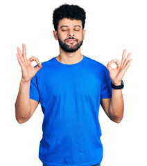 Young arab man with beard wearing casual blue t shirt relaxed and smiling with eyes closed doing meditation gesture with fingers. yoga concept.