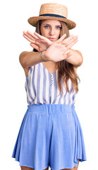 Young beautiful blonde woman wearing summer hat rejection expression crossing arms and palms doing negative sign, angry face