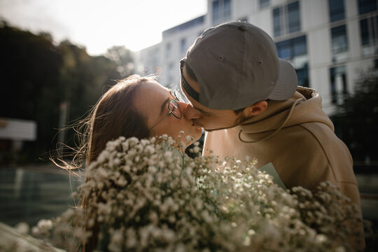 Beautiful close-up view of kissing young handsome woman and man. Blurred floral bouquet in the foreground