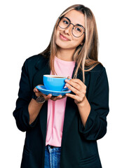 Hispanic young woman drinking a cup of coffee relaxed with serious expression on face. simple and natural looking at the camera.