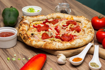Tasty pizza with pepperoni, ham and peppers and pizza ingredients around the table