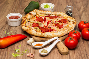 Tasty pizza with pepperoni, ham and peppers and pizza ingredients around the table