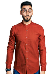 Young hispanic man with beard wearing business shirt and glasses making fish face with lips, crazy and comical gesture. funny expression.