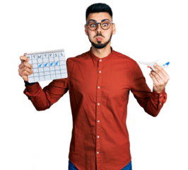 Young hispanic man with beard holding plane toy and travel calendar puffing cheeks with funny face. mouth inflated with air, catching air.