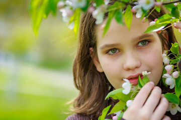 Beautiful girl among cherry flowers in spring. Portrait of a girl with brown hair and green eyes.