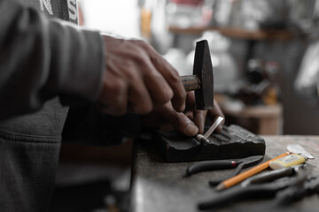 A craftsman jeweler is using a small hammer to create a jewel