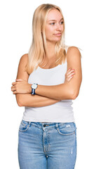 Fototapeta premium Young blonde girl wearing casual style with sleeveless shirt looking to the side with arms crossed convinced and confident