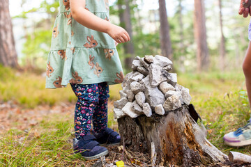 Child stacks a pile of stones. Stone tower for trail marking on tree stump. Kind stapelt einen Steinhaufen. Steinturm zur Wegmarkierung auf Baumstumpf. 