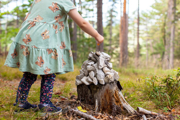Child makes a pile of stones. Stone tower for trail marking on tree stump. Kind macht einen...