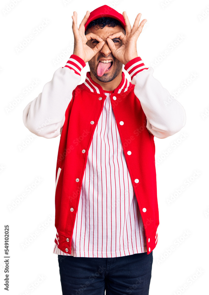 Poster young hispanic man wearing baseball uniform doing ok gesture like binoculars sticking tongue out, ey