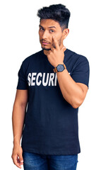 Naklejka premium Handsome latin american young man wearing security t shirt pointing to the eye watching you gesture, suspicious expression