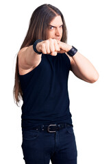 Young adult man with long hair wearing goth style with black clothes punching fist to fight,...