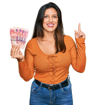 Beautiful hispanic woman holding south african 50 rand banknotes surprised with an idea or question pointing finger with happy face, number one