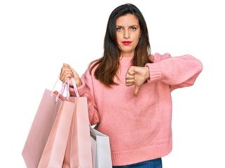 Beautiful hispanic woman holding shopping bags with angry face, negative sign showing dislike with thumbs down, rejection concept