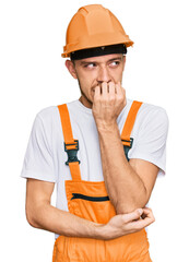Hispanic young man wearing handyman uniform and safety hardhat looking stressed and nervous with hands on mouth biting nails. anxiety problem.