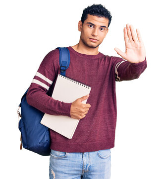 Hispanic handsome young man wearing student backpack and notebook with open hand doing stop sign with serious and confident expression, defense gesture