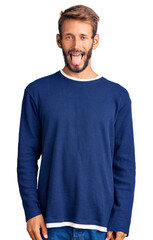 Fototapeta premium Handsome blond man with beard wearing casual sweater sticking tongue out happy with funny expression. emotion concept.