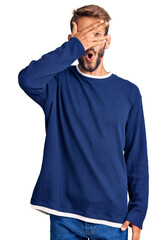 Fototapeta premium Handsome blond man with beard wearing casual sweater peeking in shock covering face and eyes with hand, looking through fingers with embarrassed expression.