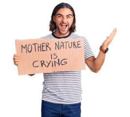 Young handsome man holding mother nature is crying protest cardboard banner celebrating victory with happy smile and winner expression with raised hands