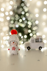 Ceramic snowman in a knitted white hat against the background of a Christmas tree