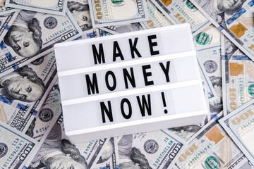 Make money now spelled in letters on lightbox on dollars background