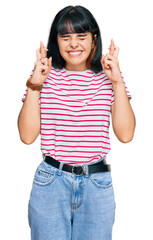 Young hispanic girl wearing casual clothes gesturing finger crossed smiling with hope and eyes closed. luck and superstitious concept.