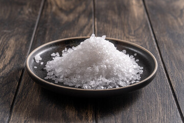 Coarse salt on dark plate on oak table closeup